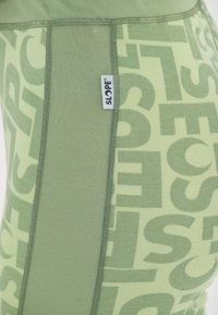 Green leggings featuring a textured design with large, contrasting letters. Includes a small label on the side.