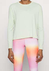 Maglietta a maniche lunghe di un verde chiaro, realizzata in tessuto morbido, con collo rotondo e vestibilità rilassata, abbinata a leggings con gradiente dal rosa all'arancione.