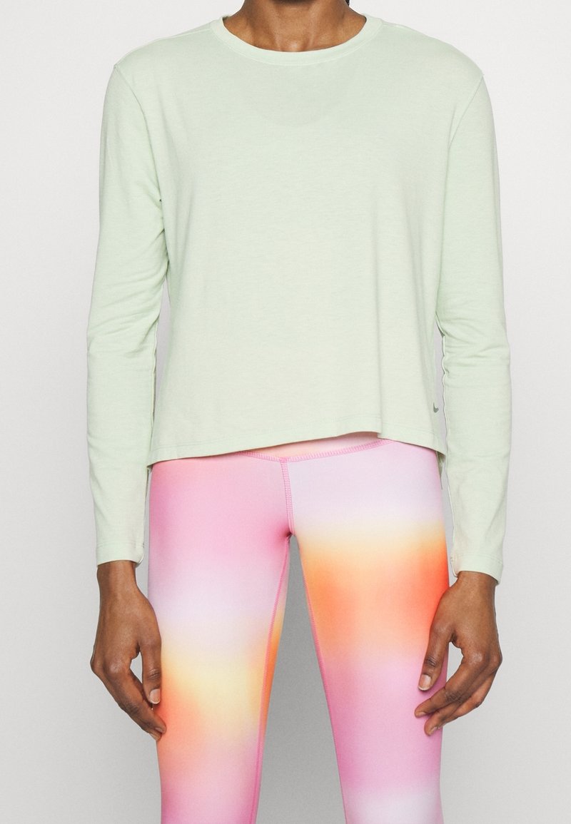 Maglietta a maniche lunghe di un verde chiaro, realizzata in tessuto morbido, con collo rotondo e vestibilità rilassata, abbinata a leggings con gradiente dal rosa all'arancione.