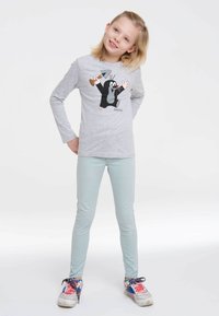 Gray long-sleeve shirt features a cartoon mole graphic, paired with light blue skinny jeans and colorful sneakers with laces.