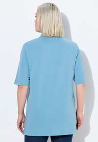 Světle modrý top s krátkým rukávem, který má volný střih, zakulacený lem a texturovanou tkaninu. Zadní část má jednoduchý, čistý design bez ozdob.