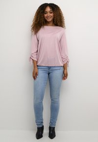 Ljust rosa långärmad topp med sidofåll, matchad med åtsittande ljusblå jeans och svarta ankelboots. Slät tygtextur.