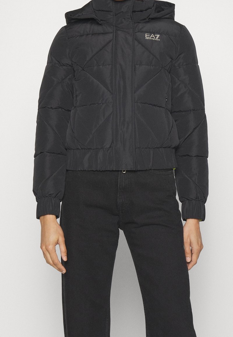 Czarna kurtka puchowa z kapturem, z przeszyciami w kształcie diamentów, elastycznymi mankietami i krótkim fasonem. Logo znajduje się na lewej piersi.