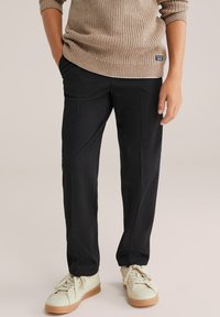 Svarta byxor med en avslappnad passform, med sidofickor och en mjuk textur, kombinerat med beige sneakers och en stickad beige tröja.