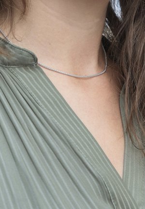 Zilveren ketting gedragen met een groen gestreept topje, die een taps toelopende kraag en textuurdetails in de stof toont.