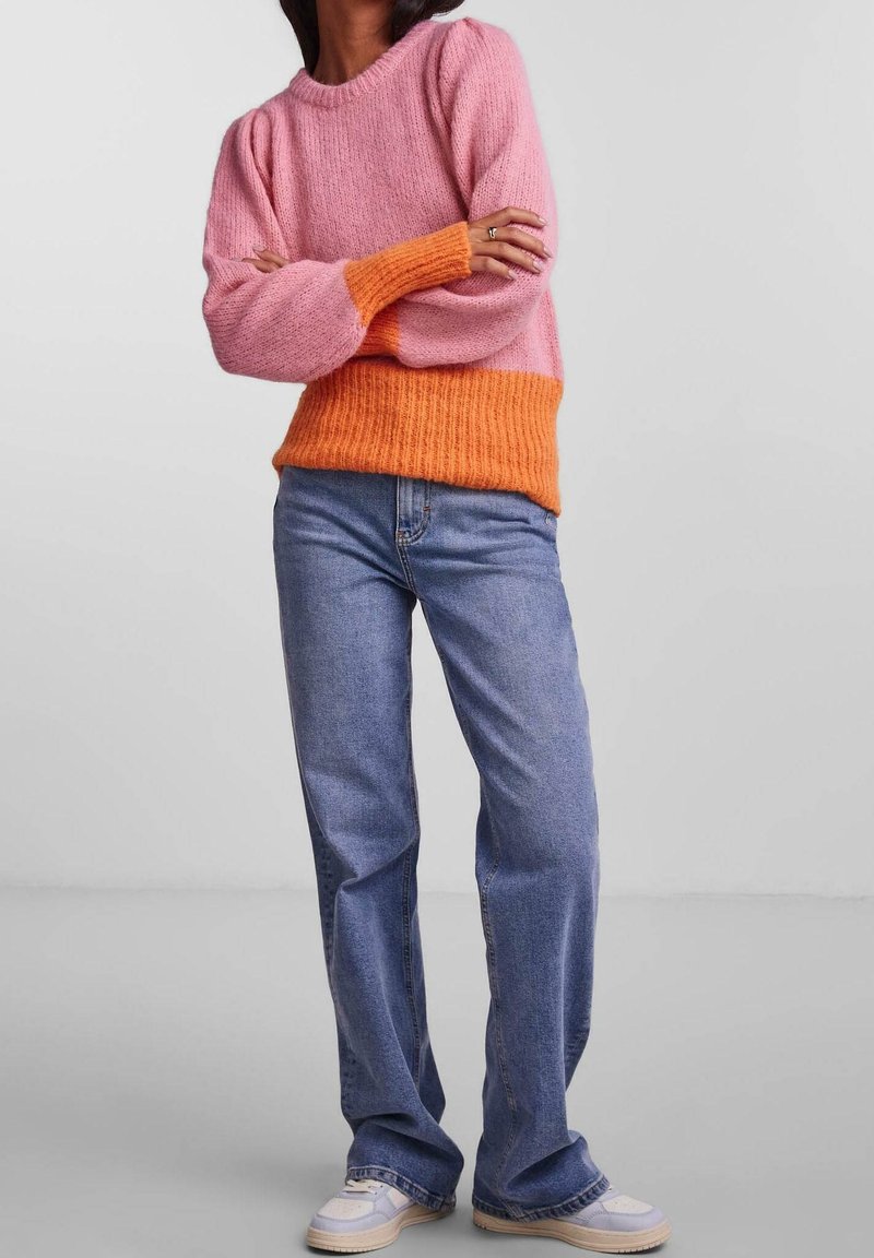 Color-blocked sweater featuring a pink top section and an orange ribbed bottom. Paired with relaxed-fit blue denim jeans and light shoes.
