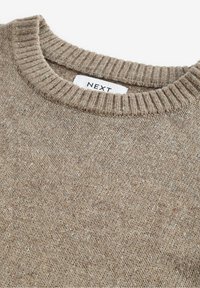 Beige gestrickter Pullover mit einem gerippten Rundhalsausschnitt, der aus einem strukturierten Stoff mit Farbflecken besteht. Das Etikett trägt die Aufschrift "NEXT."