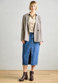 Μπεζ σακάκι καρό, ελαφρύ πουκάμισο με κουμπιά, μπλε τζην φούστα με μπροστινή σχισμή και καφέ γόβες ankle boots. Ζεστή ξύλινη επιφάνεια στο φόντο.