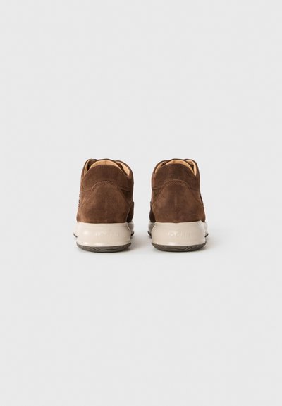 Un paio di sneaker in suede marrone con suole beige, viste da dietro, su uno sfondo bianco uniforme.