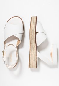 Valkoiset espadrille-sandaalit, joissa on ristiinselkädesign, sileä synteettinen materiaali ja juuttiköysistä valmistettu korko, joka lisää korkeutta.