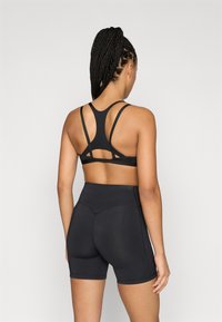 Fekete sportmelltartó keresztbe kötött hátpántokkal, magasderekú fekete rövidnadrággal párosítva, amely sima textúrájú és minimális varrási részletekkel rendelkezik.