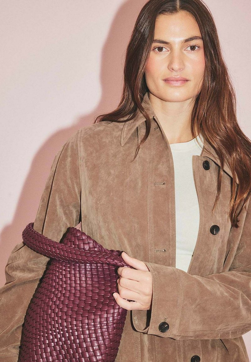 Brun mockaskinnsjacka med tydliga knapppunkter, i kombination med en vävd bordeauxväska med texturerade mönster och ett rundat handtag.