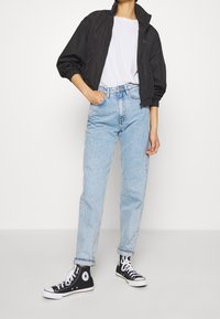 Černá bomber bunda, bílý tričko, světle modré džíny s vysokým pasem a černé kecky Converse. Neformální outfit s elastickými manžetami a ohrnutými lemy.
