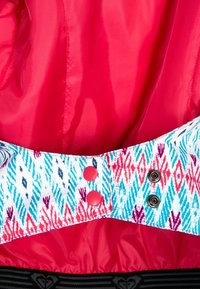 Helles rotes Gewebe mit glatter Textur; gemusterter Bund mit geometrischen Designs in Blau und Pink, gesichert mit roten Knöpfen und Druckknöpfen.