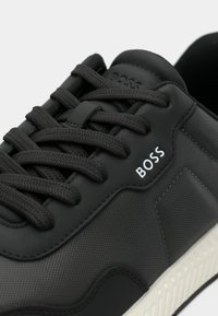 Μαύρο αθλητικό παπούτσι με υφασμένο συνθετικό επάνω μέρος, επίπεδα κορδόνια, λευκό λογότυπο "BOSS" και λευκή αντιθετική σόλα από καουτσούκ.