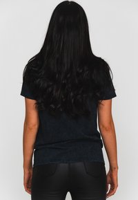 Black textured t-shirt with short sleeves, loose fit, and a curved hem. Worn with black fitted pants, showing a smooth fabric appearance.