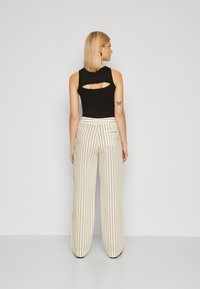 Zwarte mouwloze top met een uitgesneden achterkant, gecombineerd met crèmekleurige gestreepte broek met wijde pijpen. De broek heeft verticale strepen en een platte tailleband.