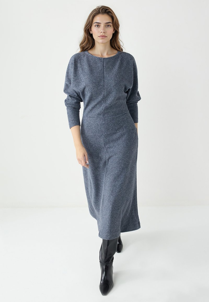 Robe longue ajustée en laine gris foncé avec un col arrondi et des manches volumineuses, associée à des bottes noires montantes jusqu'aux genoux. Texture lisse.