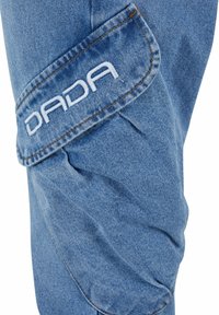 Blauer Jeansstoff mit einer strukturierten Oberfläche, ausgestattet mit einer genähten Tasche, die mit "DADA" in weißen Buchstaben bedruckt ist.