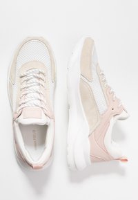 Les baskets présentent un mélange de maille blanche et de suede beige, des accents roses, des lacets ronds et une semelle rembourrée avec une languette.