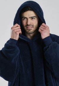 Mørkeblå fleece-hoodie med blødt, struktureret stof, stor hætte og brede ærmer. Har en afslappet pasform og ribbede manchetter.