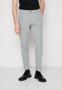 Ljusgrå chinos i bomullsblandning, slim fit, med framfickor och en knappknäppning, matchade med svarta skor.