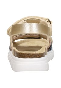 Sandal featuring a beige upper with a metallic gold strap, cork midsole, and white sole. Shows a textured design with open heel.