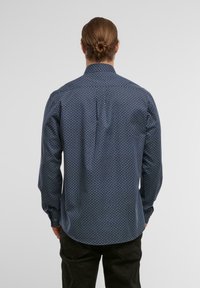 Marineblaue Langarmbluse mit geometrischem Muster, mit einem button-down Kragen und einer Rückenfalte für mehr Bewegungsfreiheit. Aus Baumwollstoff.