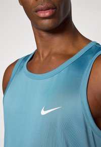 Jasnoniebieski sportowy top na ramiączkach wykonany z gładkiego, przewiewnego materiału, z białym logo Nike na klatce piersiowej oraz prostym okrągłym dekoltem.