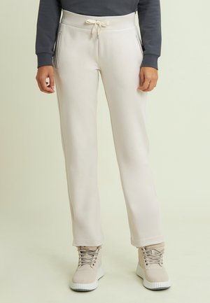 Persona che indossa pantaloni della tuta color crema con vita regolabile e tasche laterali con cerniera, abbinati a stivaletti beige con lacci.
