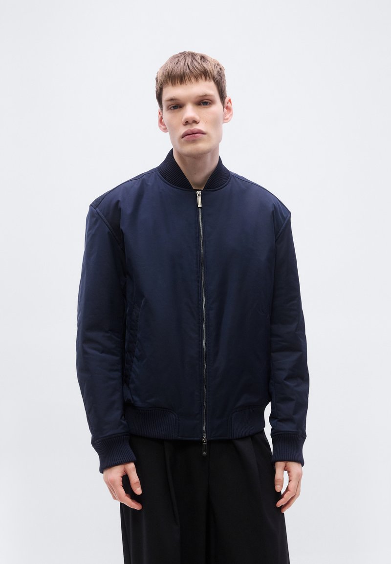 Μπλε μπουφάν bomber από απαλό ύφασμα, με φερμουάρ στο μπροστινό μέρος, ριμπ μανσέτες και τελείωμα, καθώς και πλαϊνές τσέπες.