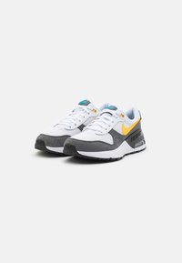 Scarpe sportive bianche in rete e suede grigio con uno swoosh giallo, accenti neri e un'unità Air visibile nella soletta, caratterizzate da dettagli testurizzati.