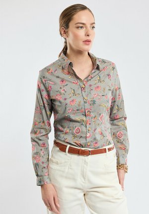 Chemise grise à boutons avec un motif floral rose et jaune, à manches longues et col classique, associée à un pantalon beige.