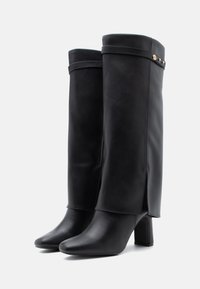 Μαύρες μπότες μέχρι το γόνατο από λείο δέρμα, με διαχωρισμένο σχέδιο, τετράγωνη σόλα και διακοσμητική ταινία με τρουκς κοντά στην κορυφή.