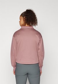 Light pink cropped jacket with a high collar, knit cuffs, and a smooth texture, paired with gray fitted pants.