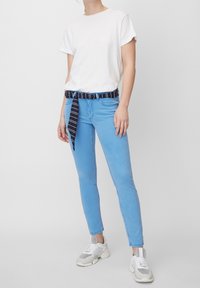 Jeans de mezclilla azul claro con un corte slim, complementados por un cinturón a rayas azul marino. Combinados con una camiseta blanca sencilla y zapatillas grises.