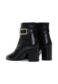 Bottes noires en cuir à chevilles avec un bout carré, un talon bloc de hauteur moyenne et un accent en boucle dorée sur la sangle de la cheville. Texture lisse, design épuré.