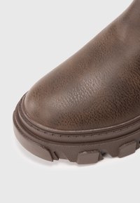 Barna, texturált bőr csizma, kerek orral, megerősített varrással és vastag, bordázott gumitalppal. Simább felület finom mintákkal.