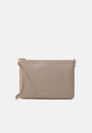 Pochette en cuir beige avec des clous dorés le long des bords, une sangle pour poignet et une fermeture éclair dorée sur fond blanc.