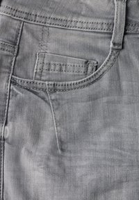 Tejido de mezclilla gris que presenta un bolsillo frontal, costuras visibles y una superficie texturizada con un aspecto ligeramente desgastado.