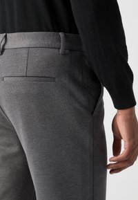 Sive po meri krojene hlače iz gladkega, raztegljivega blaga. Imajo stranske žepe, zadnji žep z ozkim robom in oprijet pas.