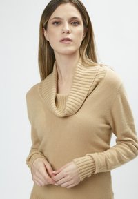 Beiger Pullover mit einem gerippten, Cowl-Ausschnitt und gerippten Bündchen. Die weiche Textur, das taillierte Design und die langen Ärmel unterstreichen den modernen Look.