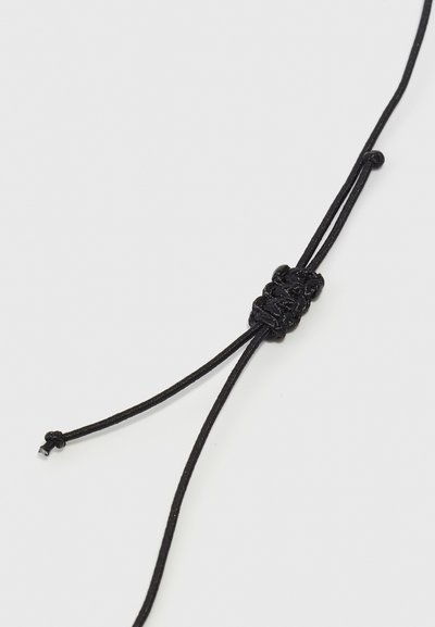 Bracelet en cordon noir avec un détail central en nœud tressé, offrant une longueur ajustable et une texture lisse. Design simple avec une esthétique minimaliste.