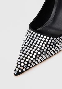 Crna cipele s šiljastim vrhom prekrivene srebrnim rhinestones, s glatkom teksturom i elegantnim dizajnom. Akcentni detalji unapređuju vizualnu privlačnost.
