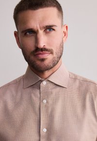 Light brown woven shirt with a structured collar, featuring a subtle texture and three white buttons down the front.