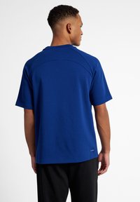 Kungsblå t-shirt med kort ärm, slät struktur, rund halsringning och böjda axelsömmar, kombinerad med svarta byxor.