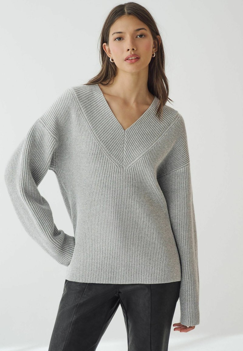 Grauer gerippter Strickpullover mit tiefem V-Ausschnitt und langen Ärmeln, der strukturierte Akzente an den Schultern und eine lockere Passform aufweist.