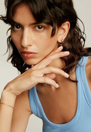 Pendientes de oro con forma de estrella, un collar de cuentas colorido y una camiseta de tirantes azul con ribetes; el modelo tiene el cabello oscuro de longitud media y piel clara.