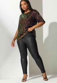 Top nero con paillettes e motivi ondulati multicolori, maniche corte, abbinato a pantaloni in ecopelle neri e tacchi a strappi neri.
