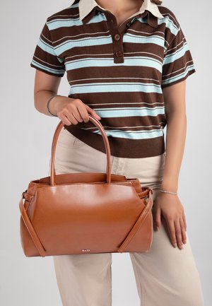 Personne portant une chemise rayée marron et bleu clair tenant un grand sac à main en cuir marron avec des doubles poignées et des bandoulières.